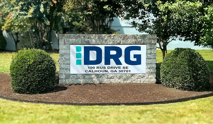 DRG sign on a stone monument at 100 Rus Drive SE, Calhoun, Georgia, framed by shrubs.