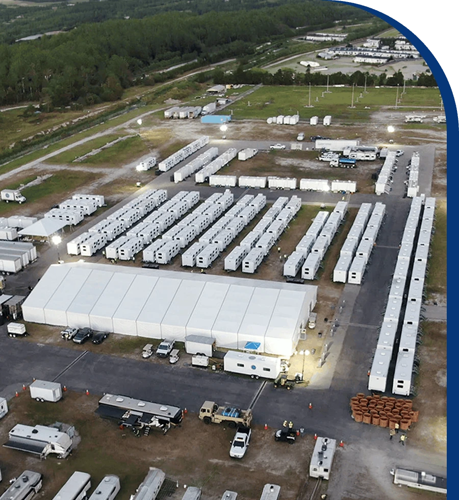 Aerial view of a large staging yard with rows of trailers and a white event tent at dusk.