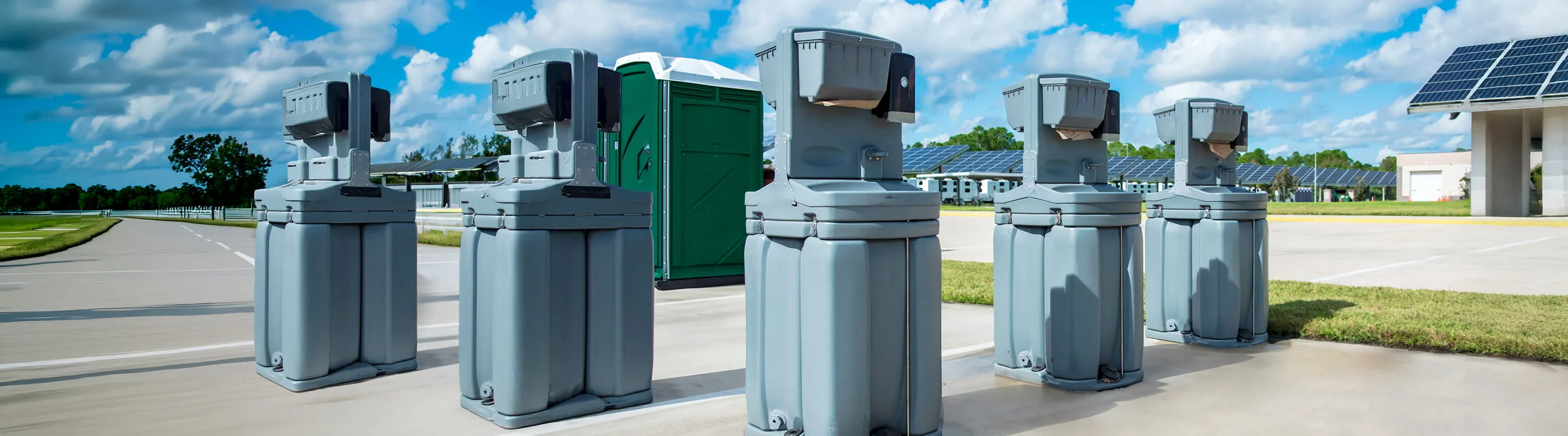 Grey portable hand wash and sanitizer stations lined up on a paved lot.