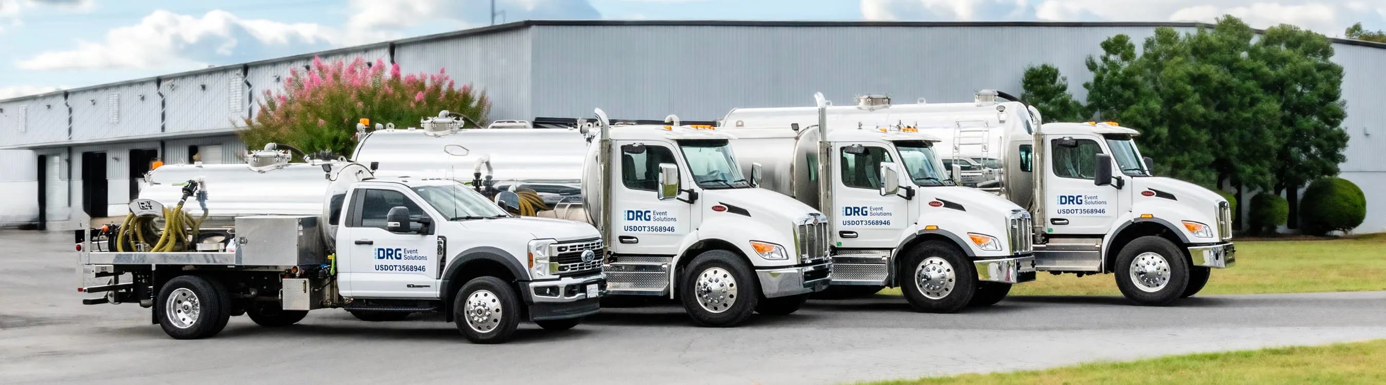 A row of white DRG service trucks and tankers parked outside a warehouse.