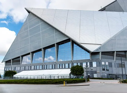 Modern stadium with an angular silver roof and a long white event tent beside it.