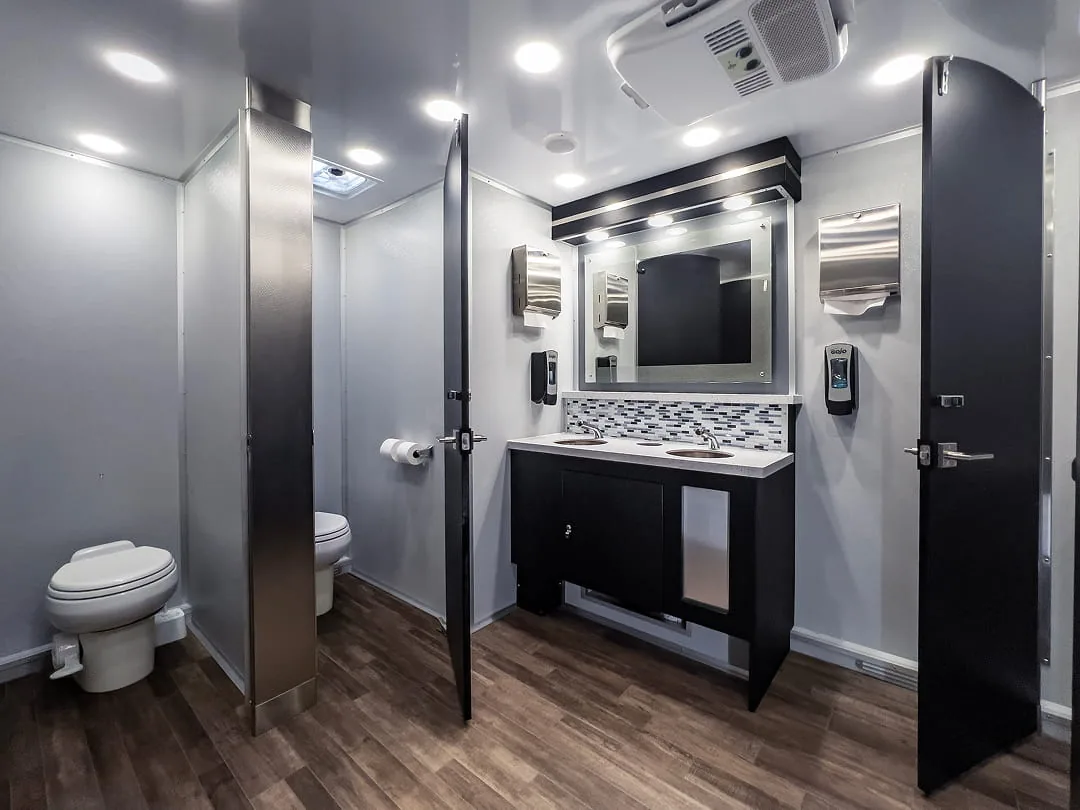 Restroom trailer interior with a toilet stall, vanity, lighted mirror, and dark wood-look floors.