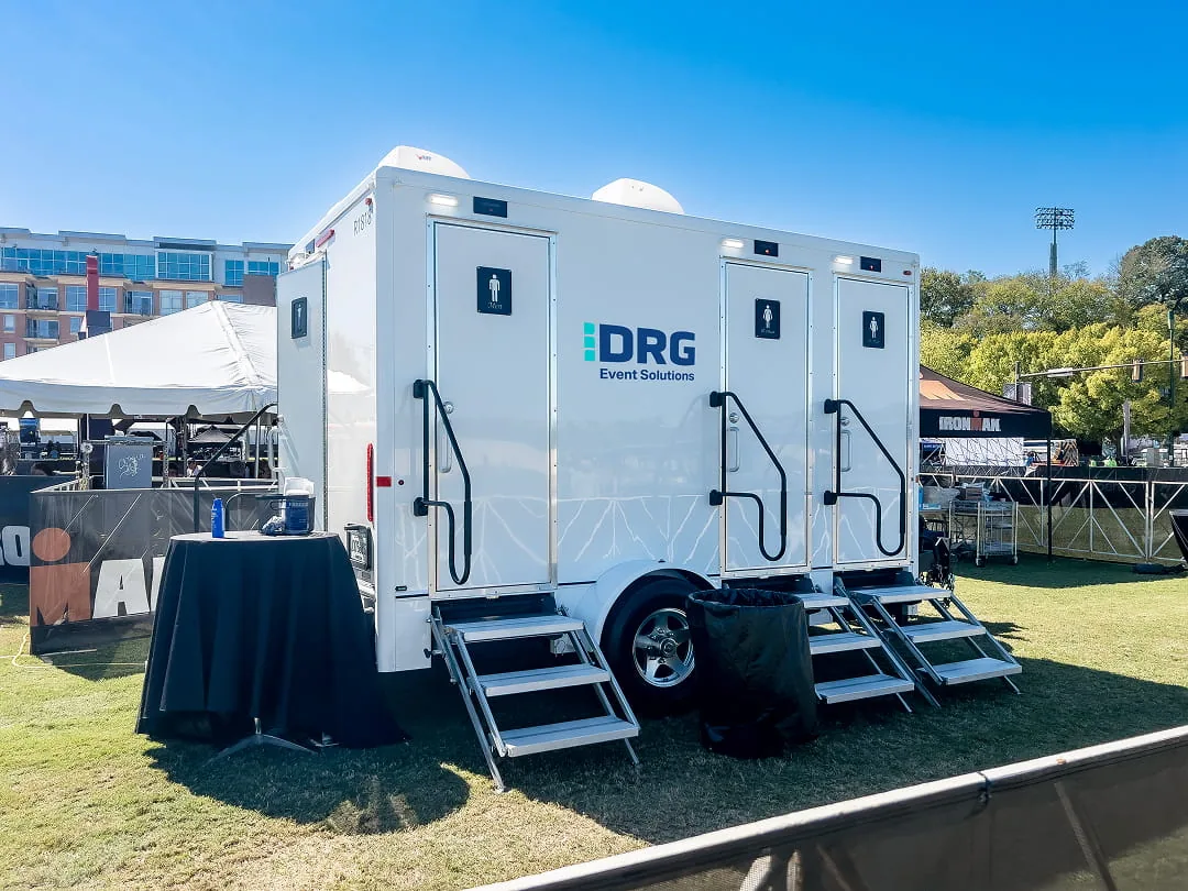 DRG Event Solutions restroom trailer with stairs and skirting set up on grass at an outdoor event.