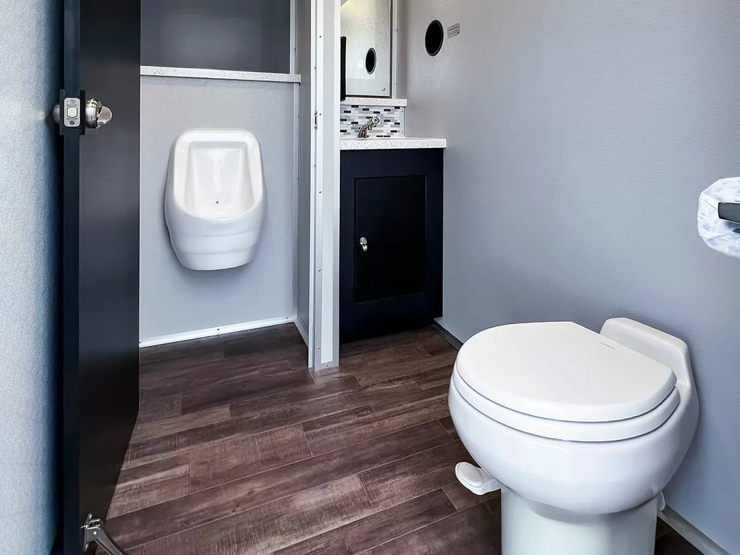 Restroom trailer interior with a urinal, a toilet, and dark wood-look floors.