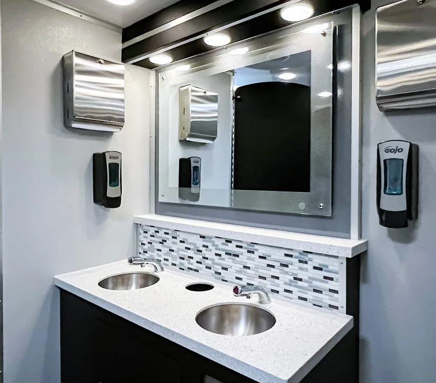 Double stainless steel sinks with a lit mirror.